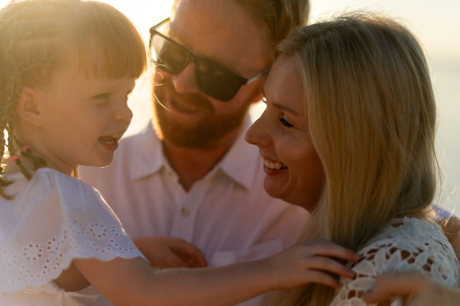 Happy family with young daughter sharing a joyful moment together on a sunny beach at golden hour.