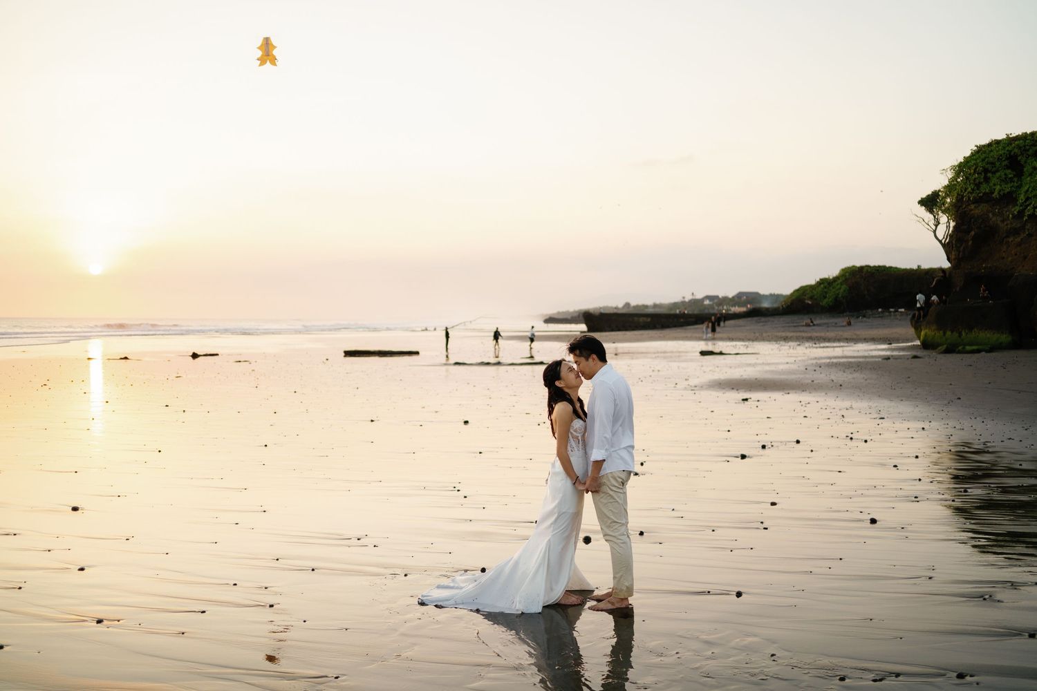 Couple in wedding attire sharing a romantic moment on a reflective beach at golden sunset.