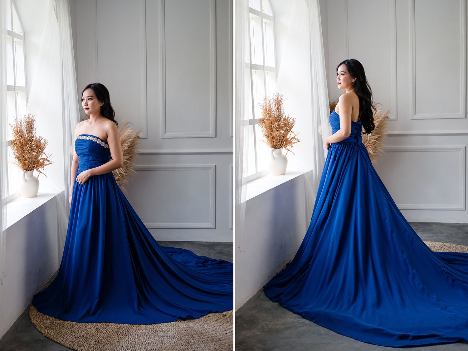 Woman in royal blue strapless satin gown with long train standing by bright window.