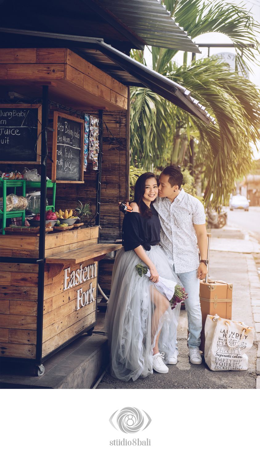 Romantic couple embracing outside Eastern Fork wooden cafe stall in Bali, woman in grey tulle skirt.