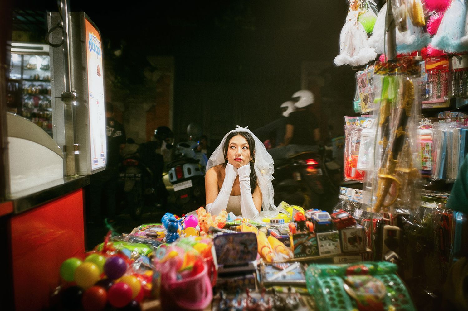 Beautiful bride in white gown and veil posing dreamily at a colorful candy market stall.