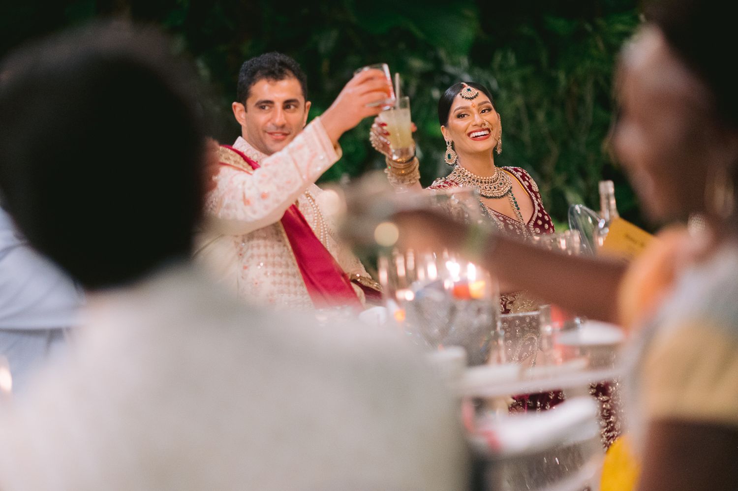 Bride and groom raise glasses in a toast at their vibrant Indian wedding reception dinner celebration.