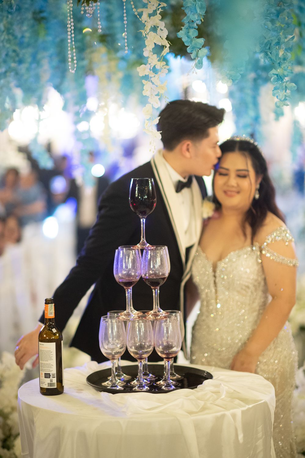 Bride and groom kissing beside a champagne glass tower at an elegant wedding reception with blue floral decorations.