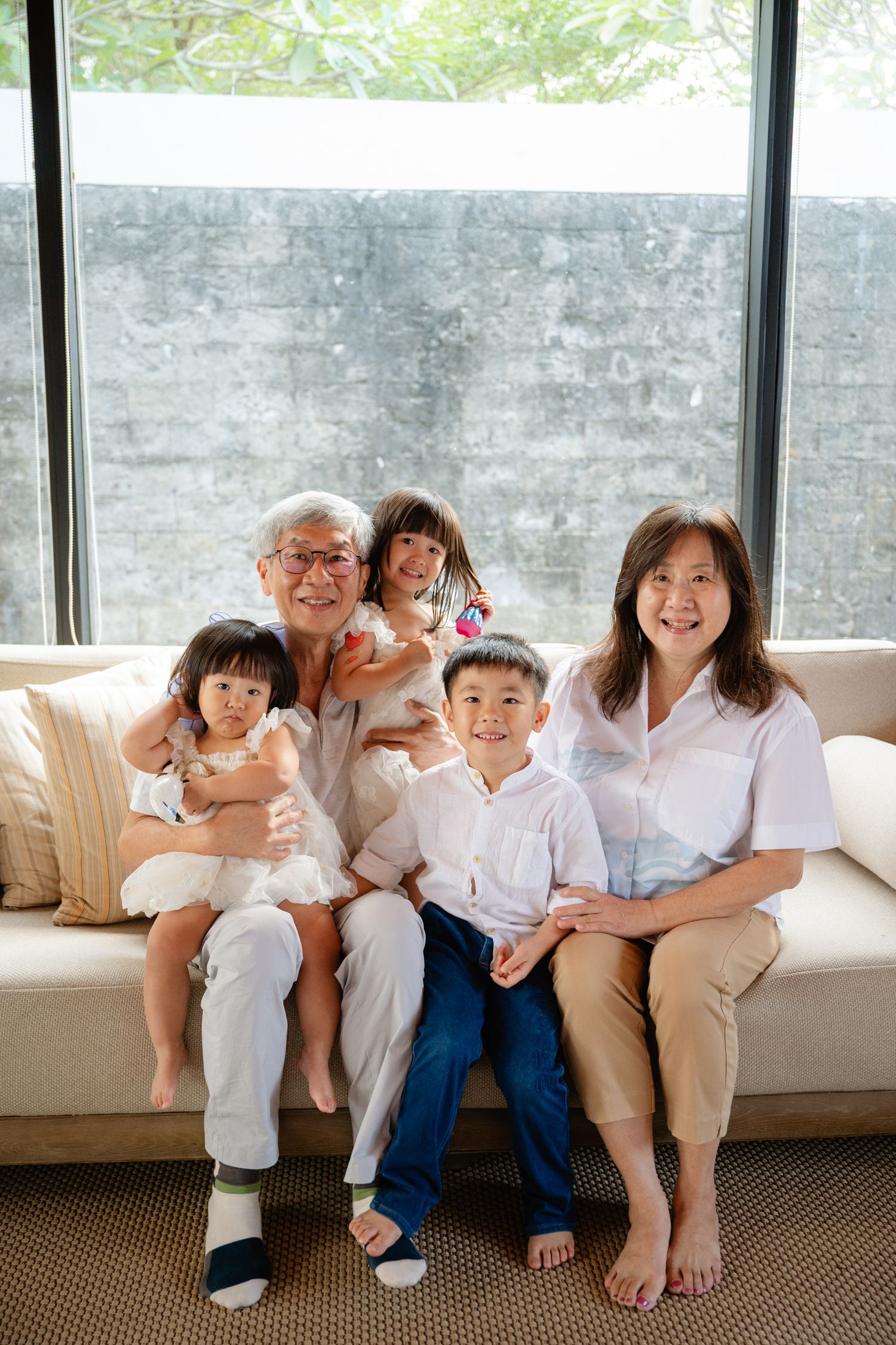 Multi-generational Asian family smiling together on a white sofa, grandparents with three young grandchildren.