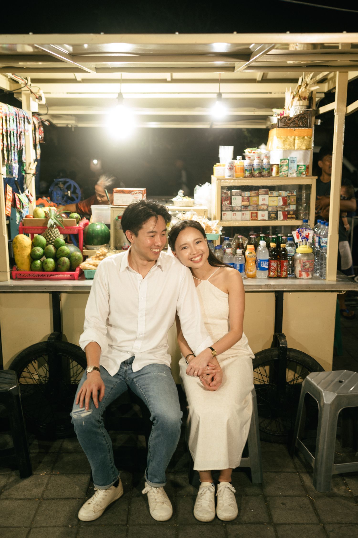 Happy couple sitting together in front of a glowing night market vendor stall.