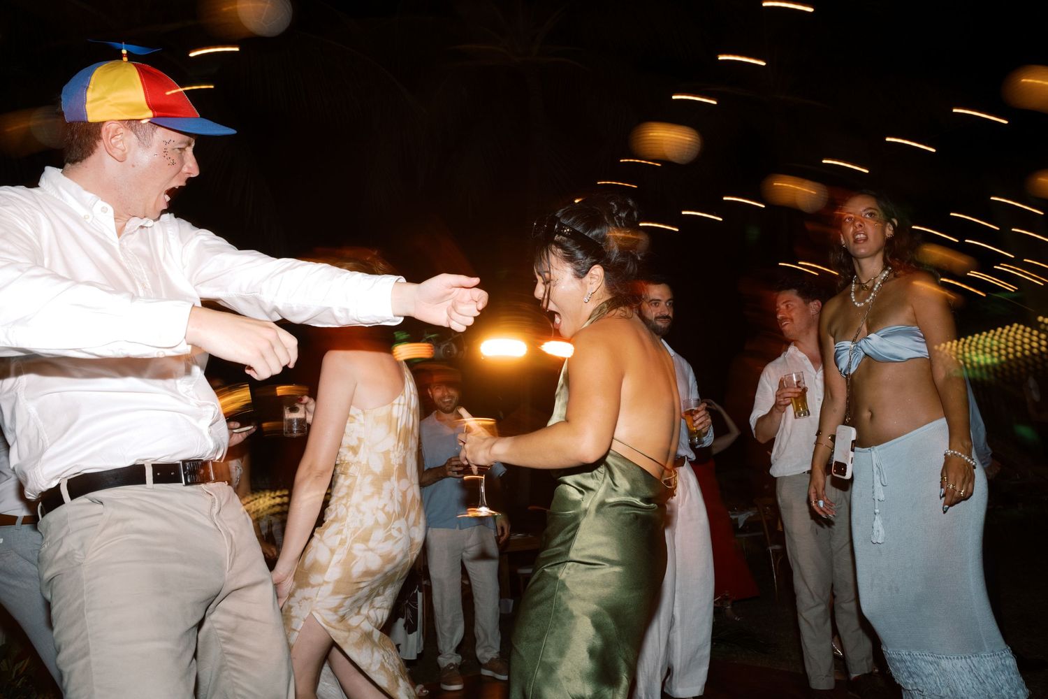 People dancing and socializing at an outdoor evening party, wearing colorful summer outfits.