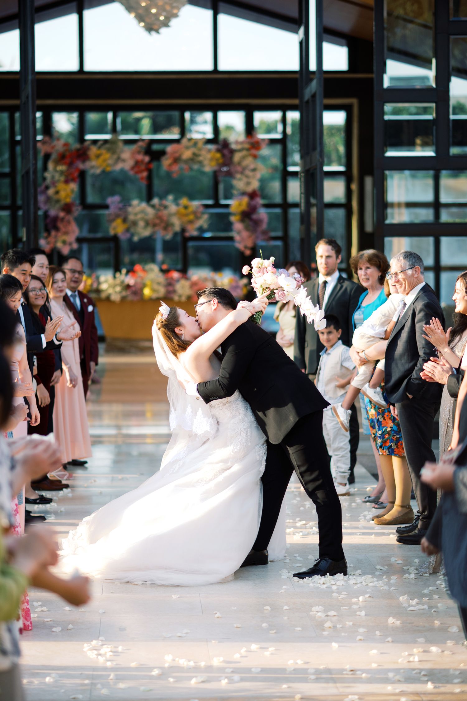 Groom dips bride for a kiss at wedding ceremony while guests applaud along the aisle.