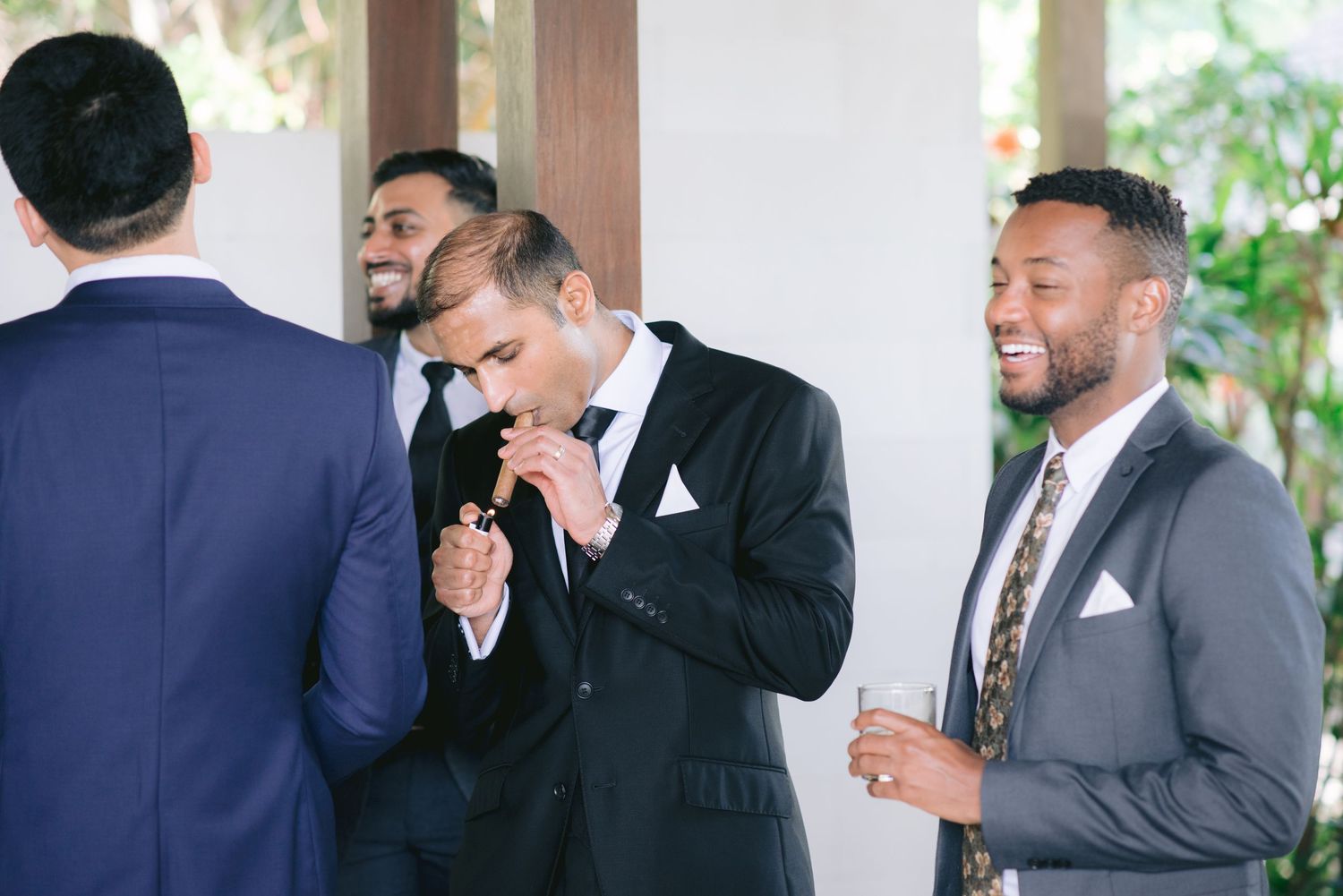 Groomsmen in suits laughing and socializing together at a wedding reception in an elegant venue.