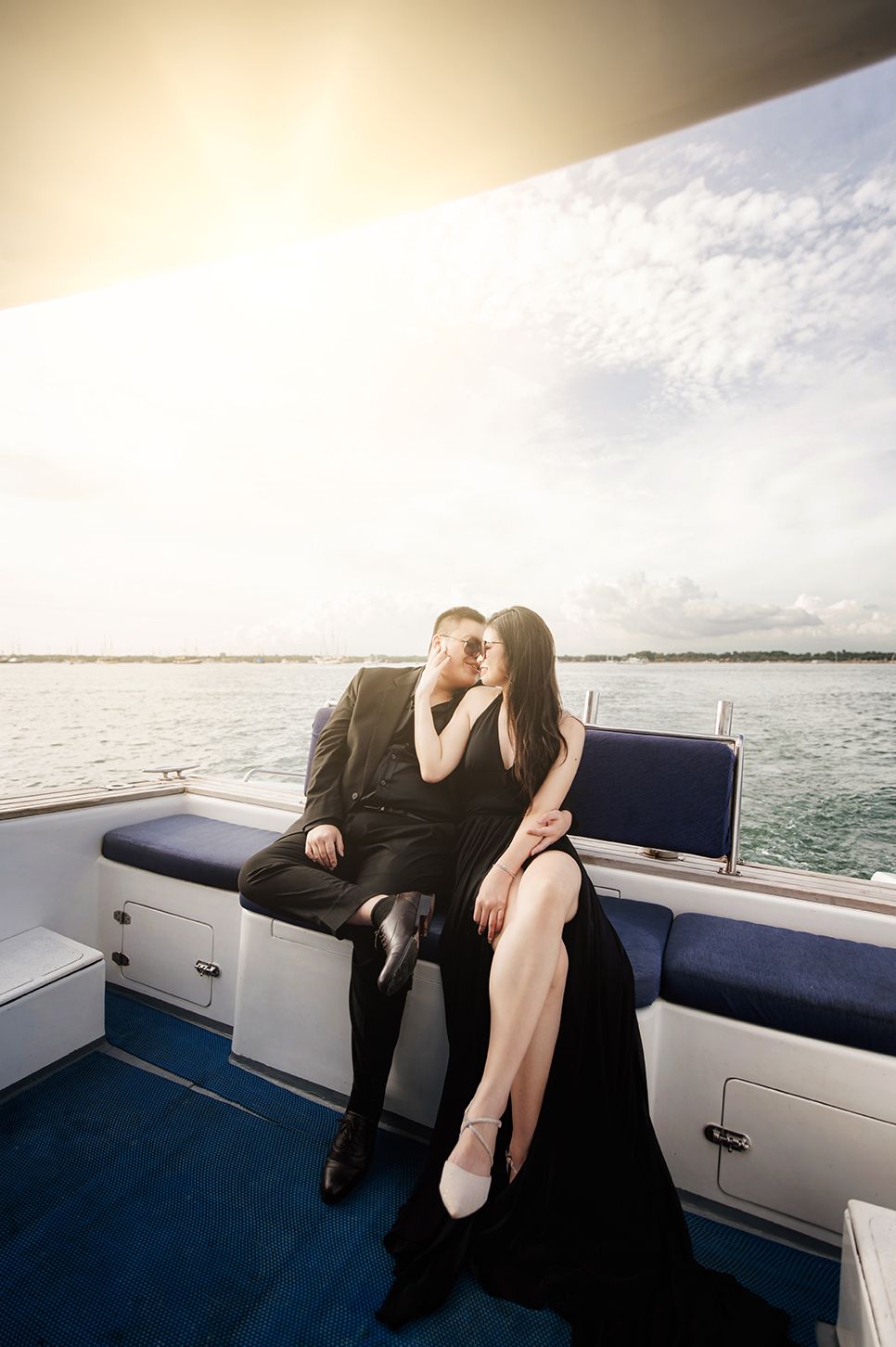 Couple in black attire sharing a romantic kiss on a luxury yacht deck with ocean views.