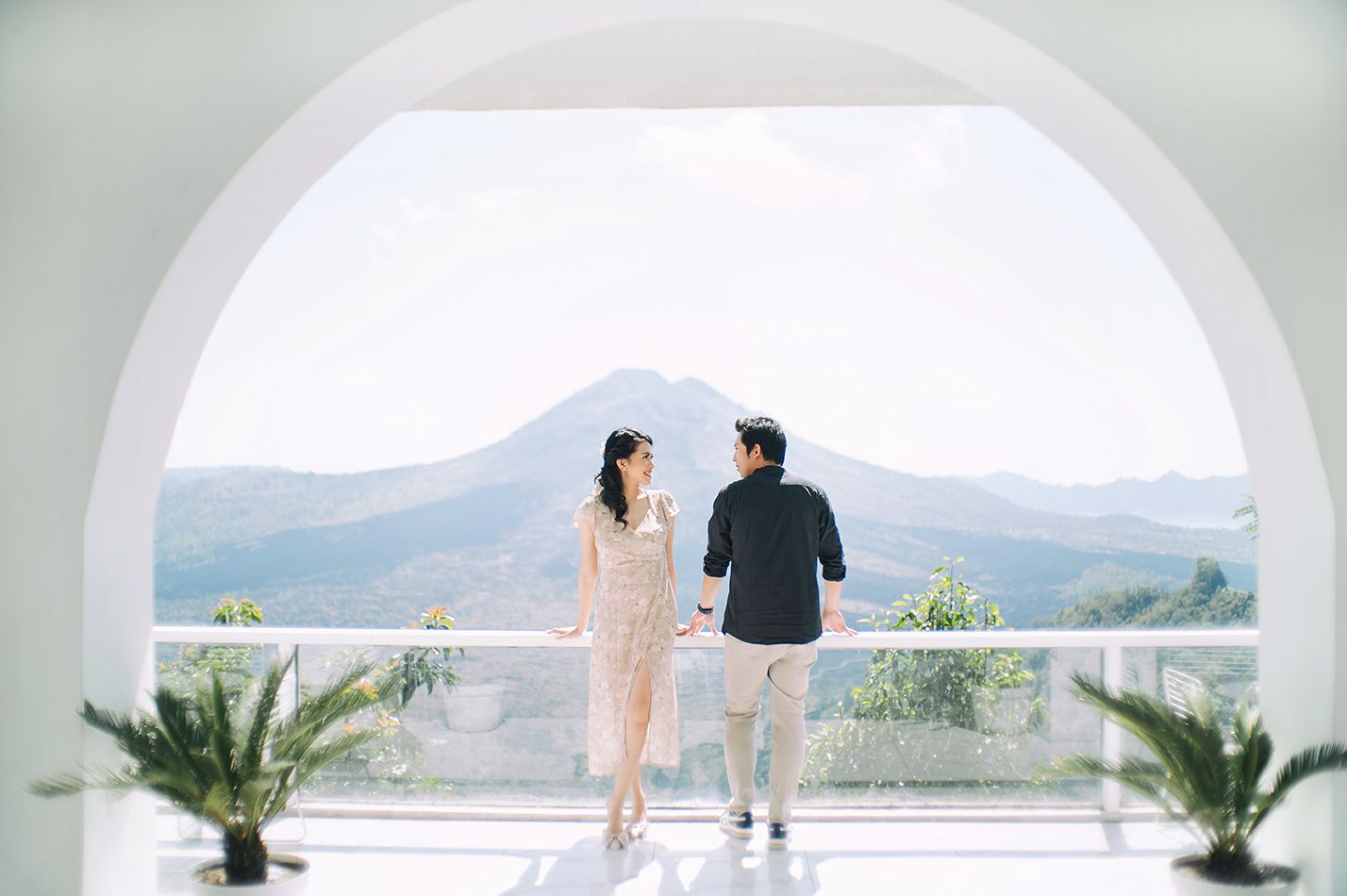 Couple walking hand in hand on a white terrace with stunning mountain and volcano views in the background.
