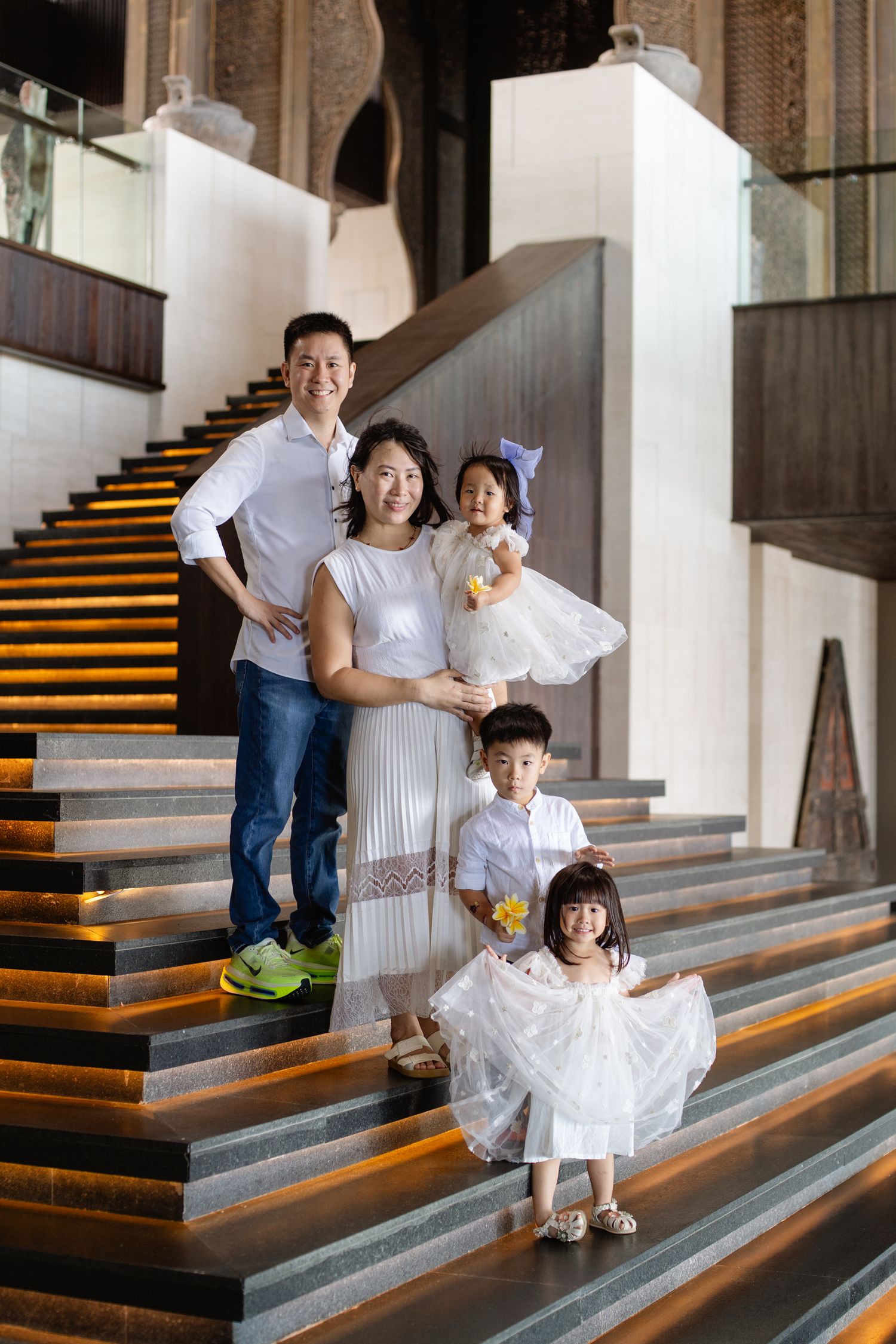 Asian family of five posing on grand staircase, parents with three young children dressed in white outfits.