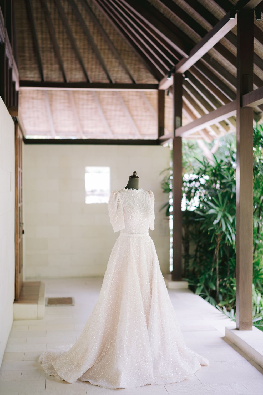 Elegant white lace wedding gown displayed on a mannequin in a serene open-air Balinese pavilion.