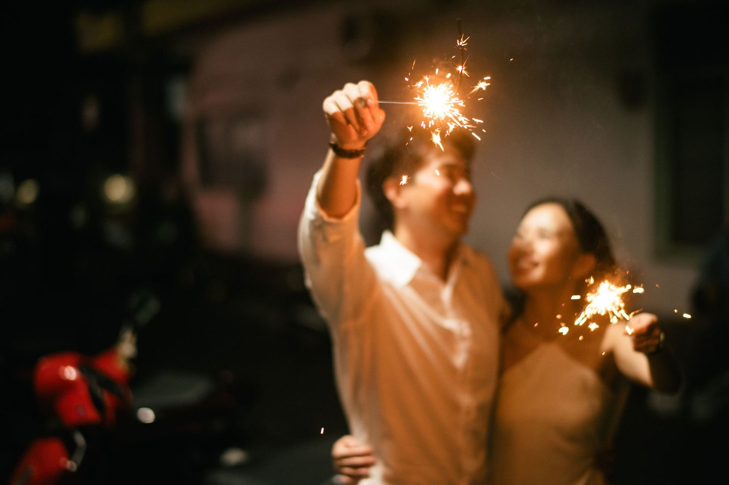 Couple holding sparklers at night, celebrating with glowing fireworks in a romantic outdoor setting.