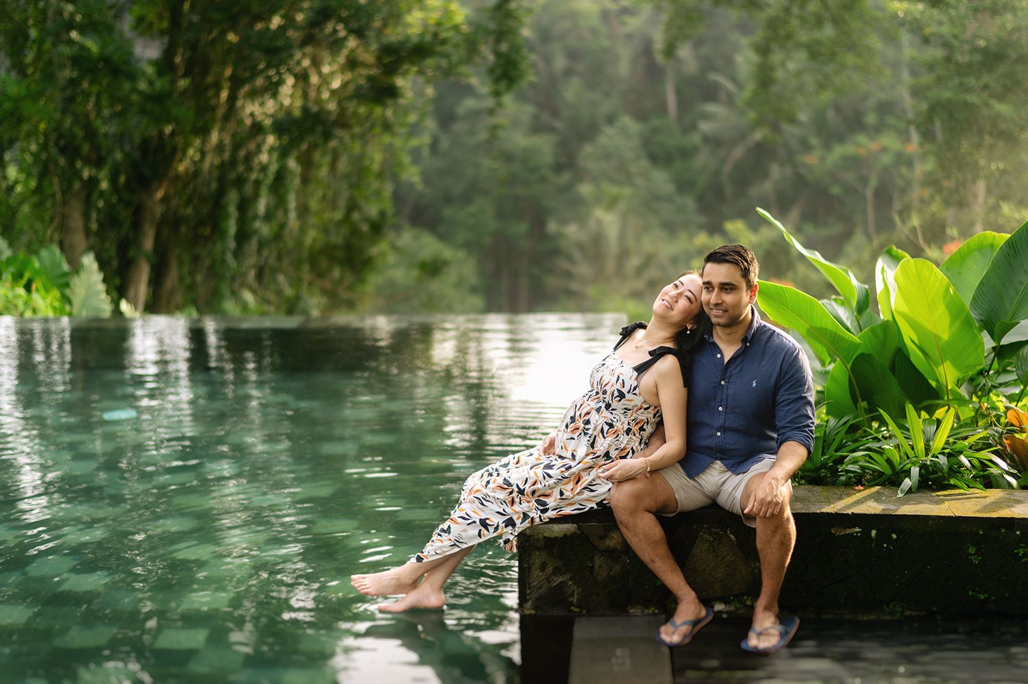 Couple sitting together by a lush tropical infinity pool surrounded by green jungle foliage Maya Ubud Resort and Spa in Bali.