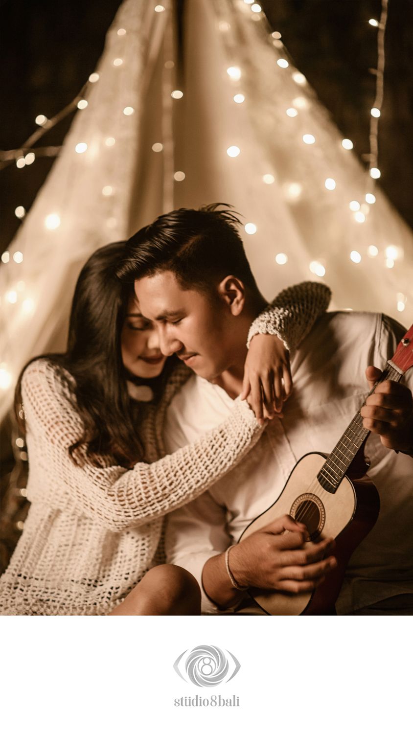 Couple sharing a romantic moment with a ukulele inside a glowing fairy light tent canopy.