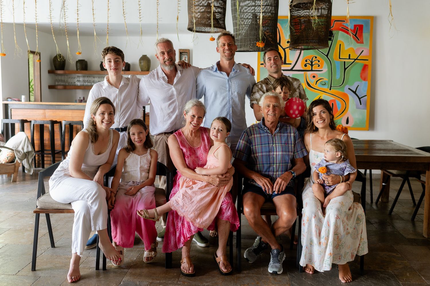 Large multigenerational family posing together indoors, smiling for a group portrait in a bright, art-decorated room.