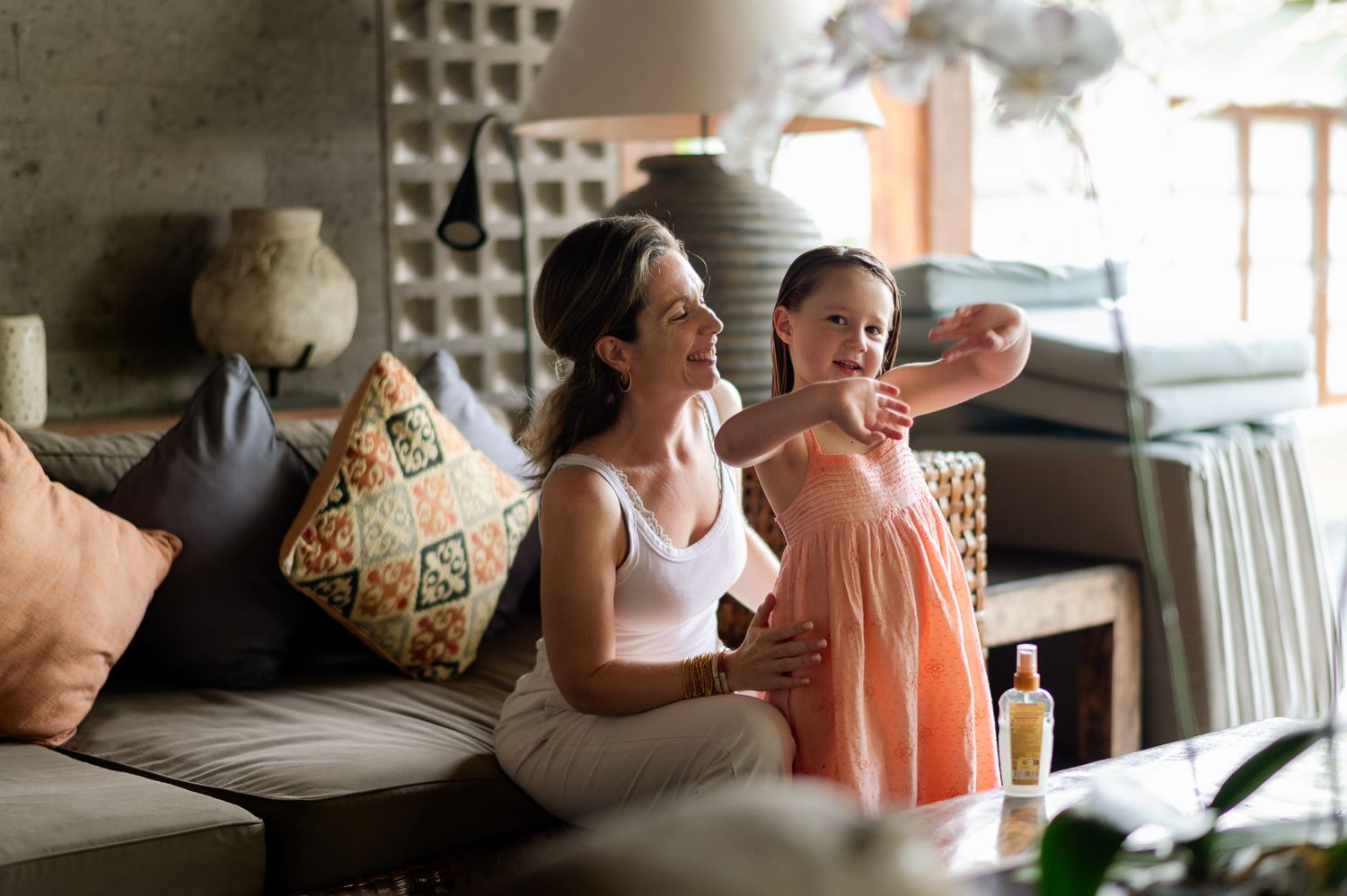 A smiling woman and young girl sit together on a couch in a cozy living room, sharing a joyful moment.