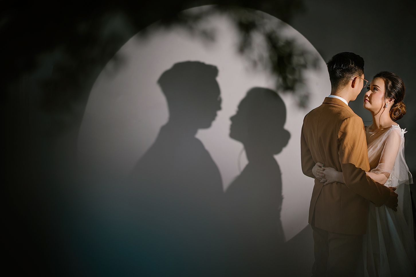 Romantic wedding couple embracing with dramatic shadow silhouettes projected on circular moonlit backdrop.