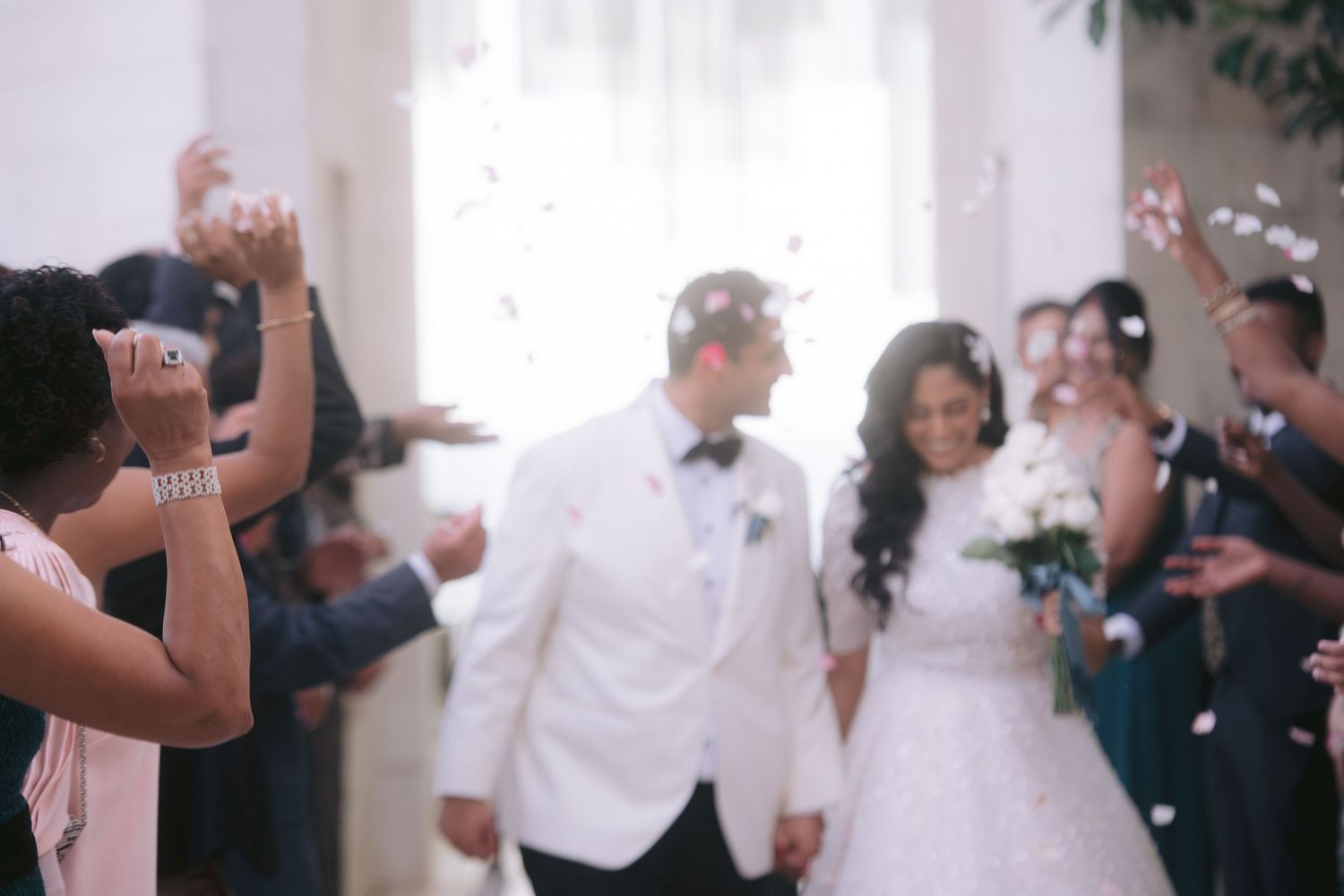 Bride and groom walk through confetti shower surrounded by cheering guests at elegant wedding reception.