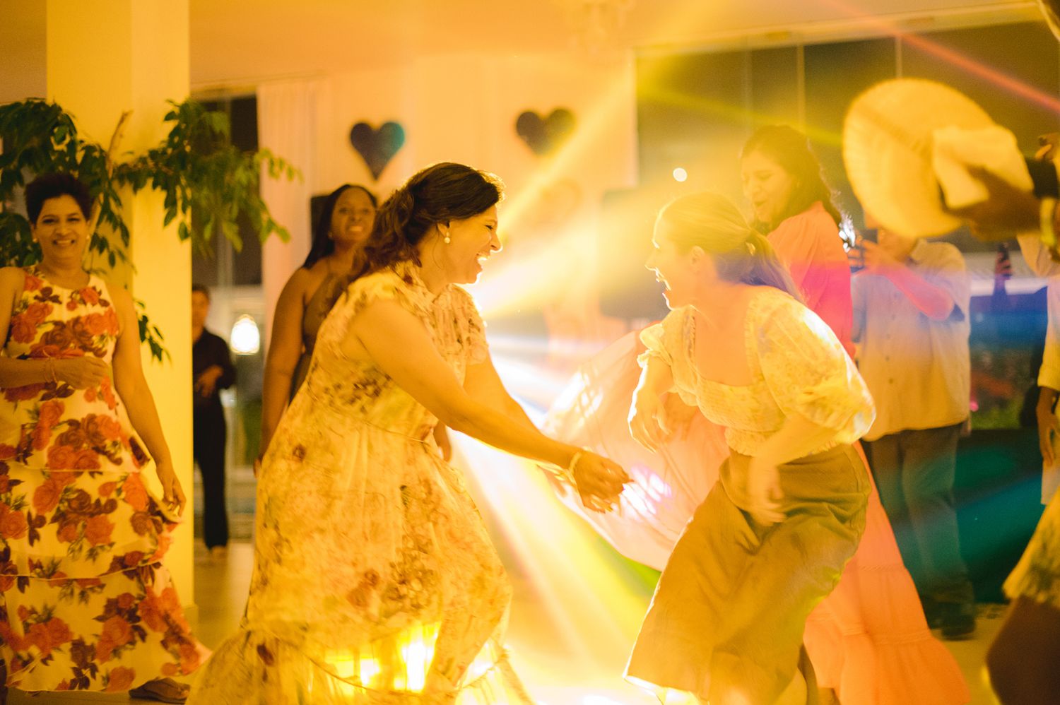 Two women dancing joyfully at a wedding reception under warm golden lights.