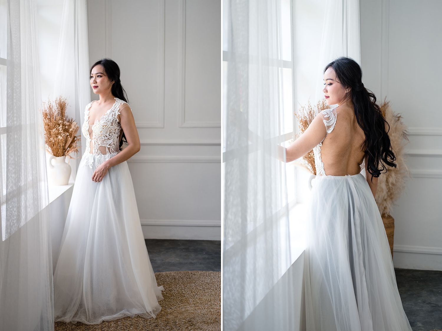 A bride in a white lace and tulle backless wedding gown poses by a sunlit window in an elegant room.