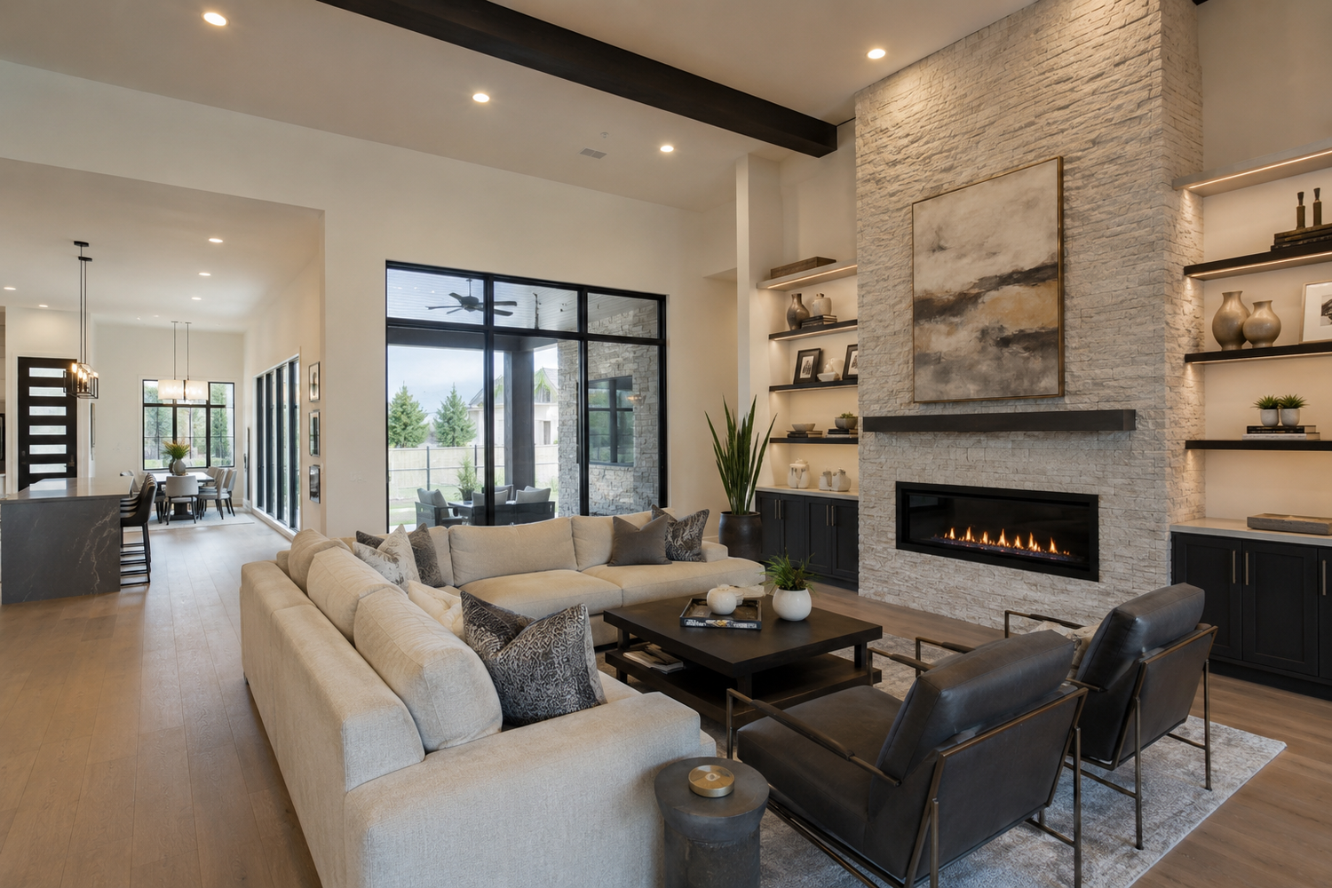 Modern open-concept living room with stone fireplace, built-in shelves, neutral sofas, and floor-to-ceiling windows.