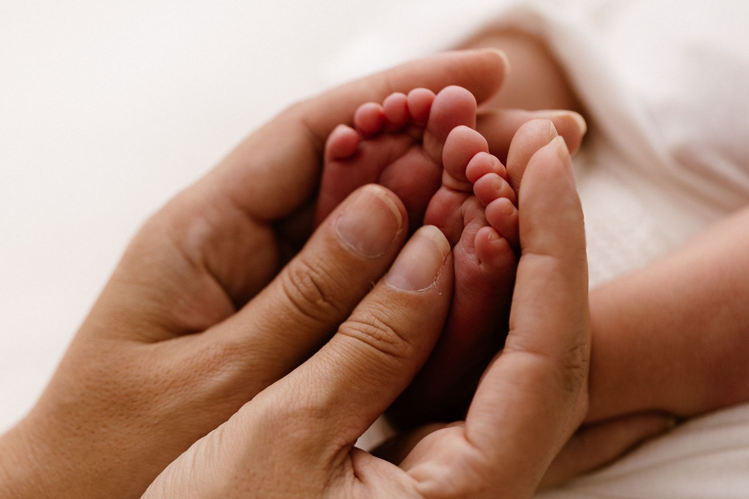 Adult hands gently cradling tiny newborn baby feet, showcasing a tender moment of parental love and care.
