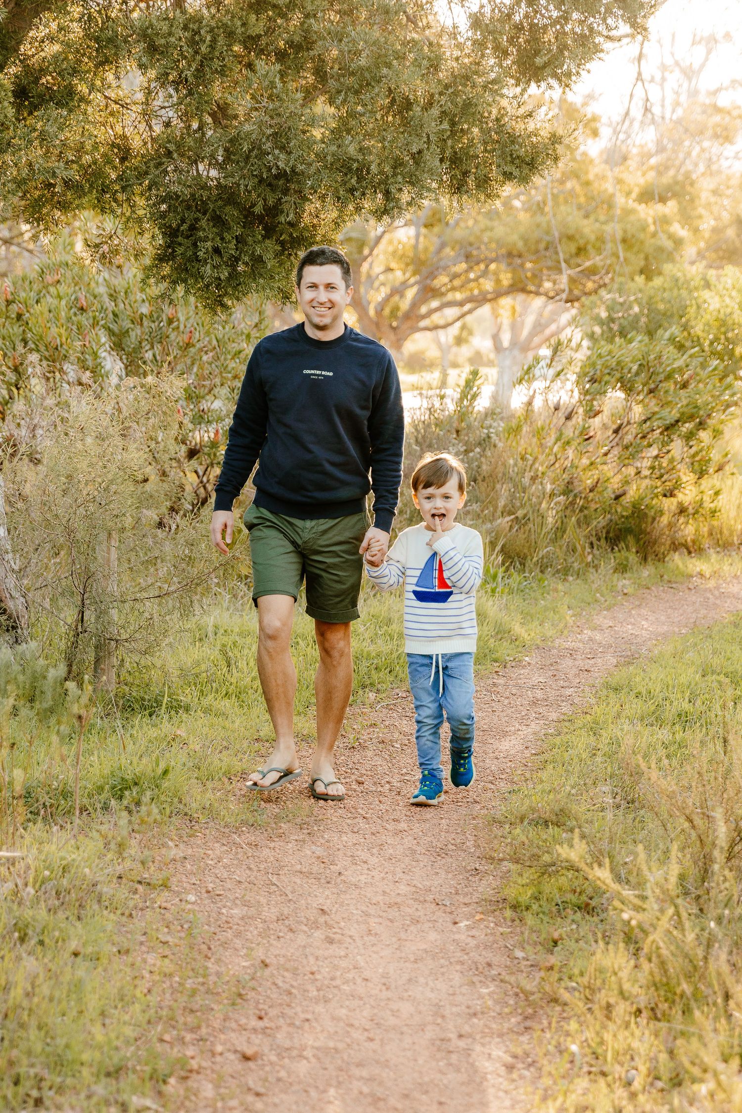 Father and young son walking hand in hand along a scenic nature path.