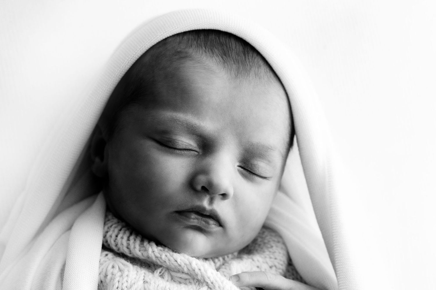 Black and white close-up portrait of a peaceful sleeping newborn baby wrapped in a soft white blanket.