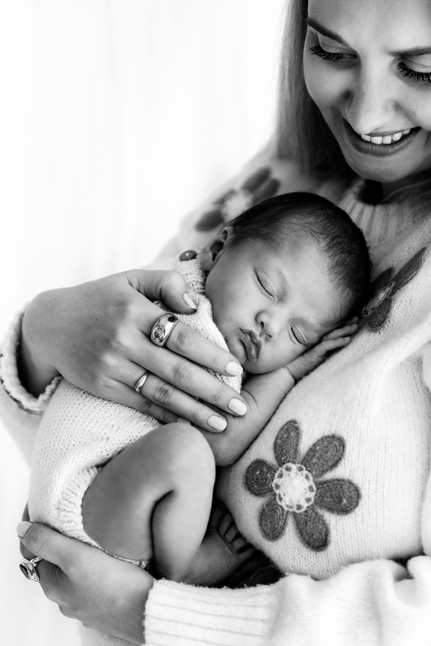 Black and white portrait of a smiling mother tenderly holding her sleeping newborn baby close.