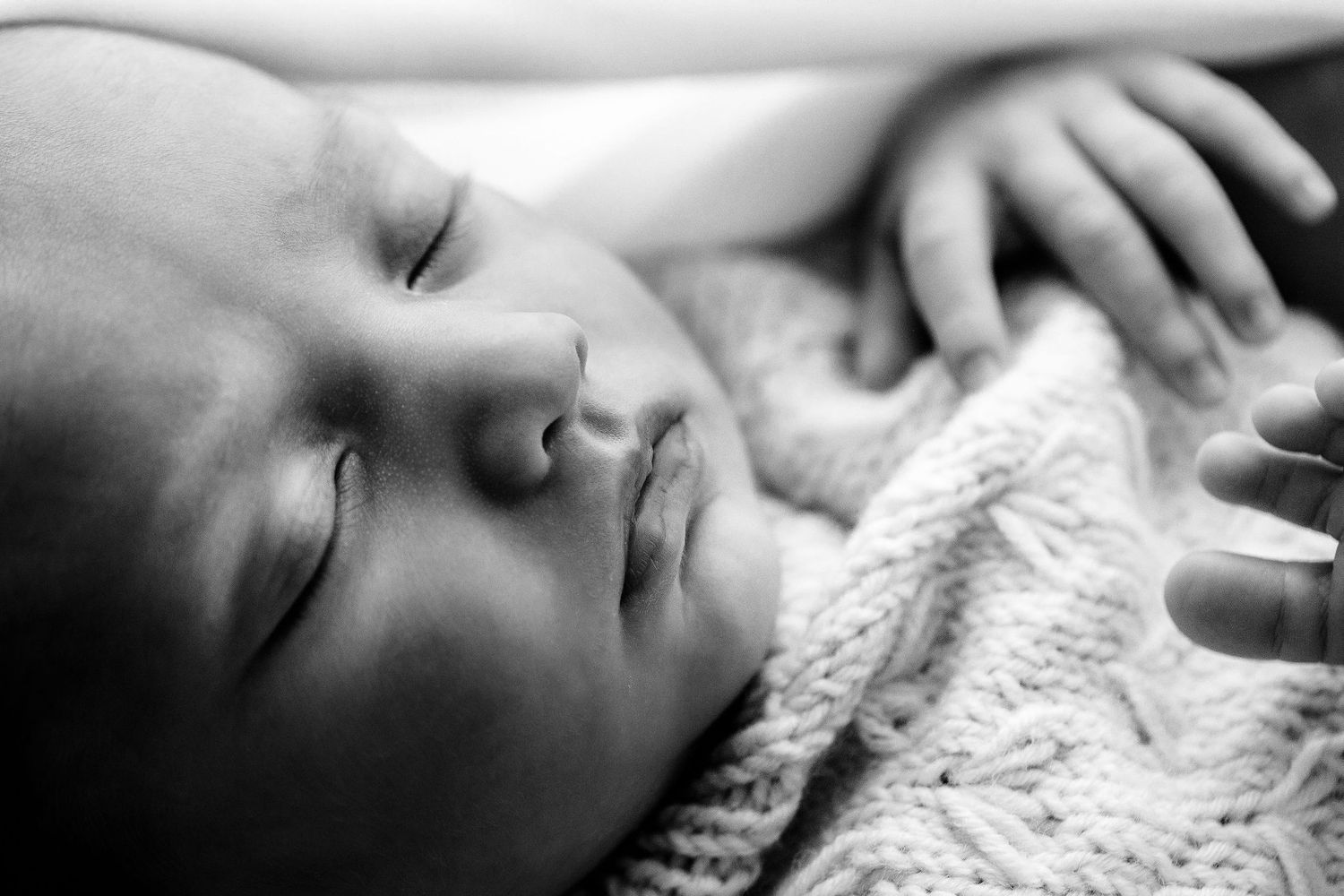 Black and white close-up of a serene sleeping newborn baby's face with soft knit blanket.