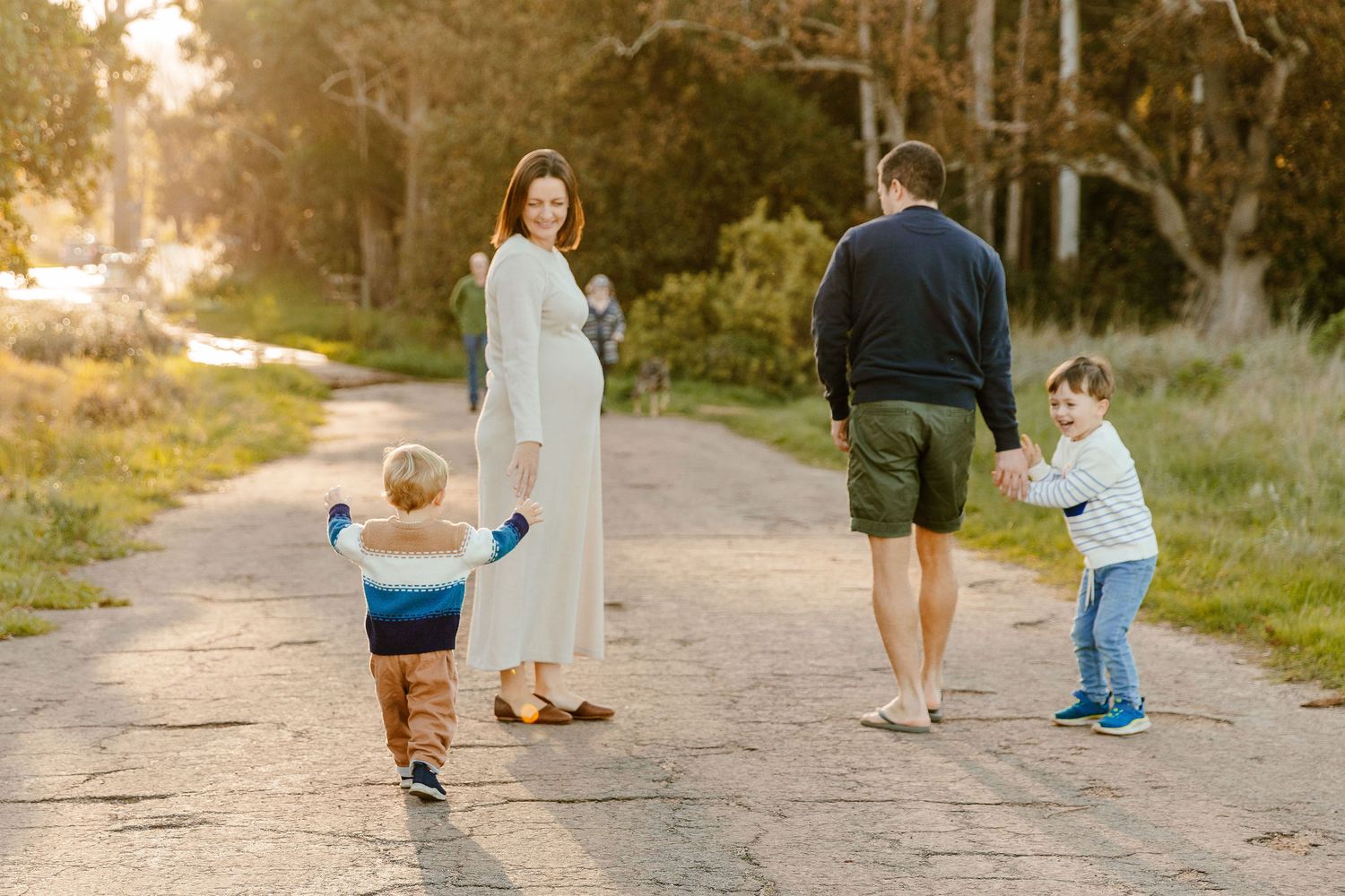 A pregnant mother and father walk a dirt path with their two young children at golden hour.