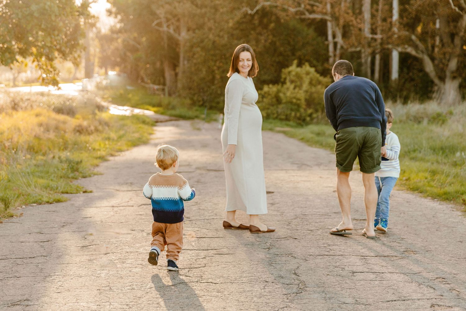 Family of four walking on a sunny dirt road during a golden hour maternity photo session.