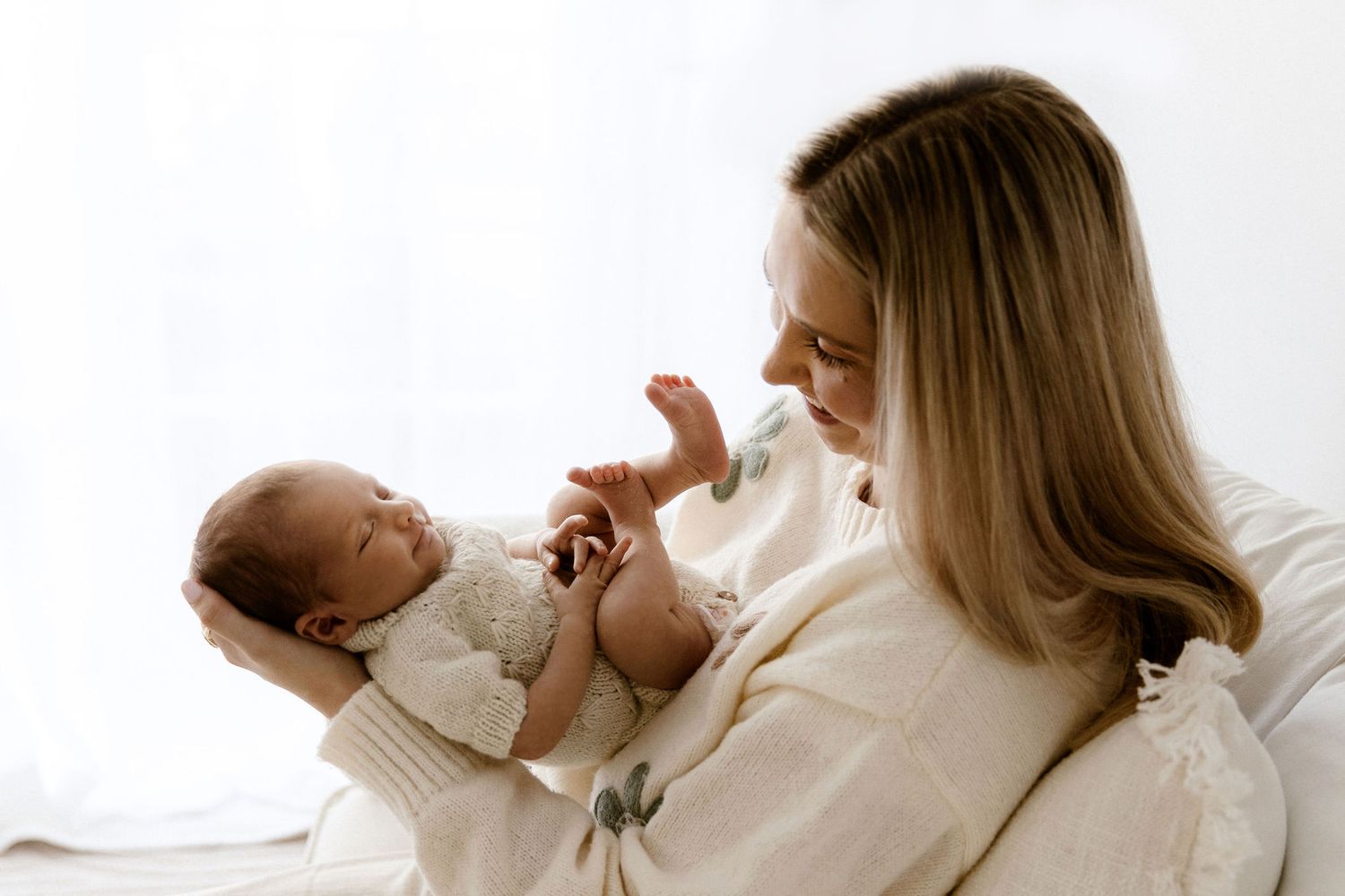 Mother tenderly holding and gazing at her sleeping newborn baby in soft light.