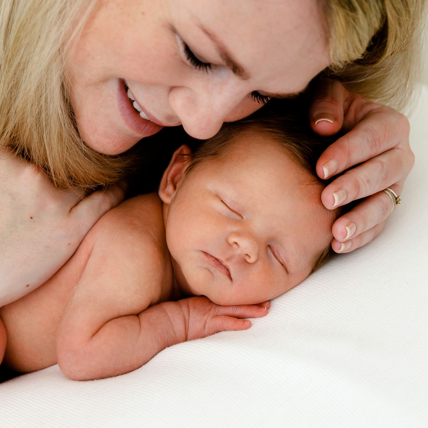 An intimate portrait of parent and newborn sharing a gentle moment on white bedding.