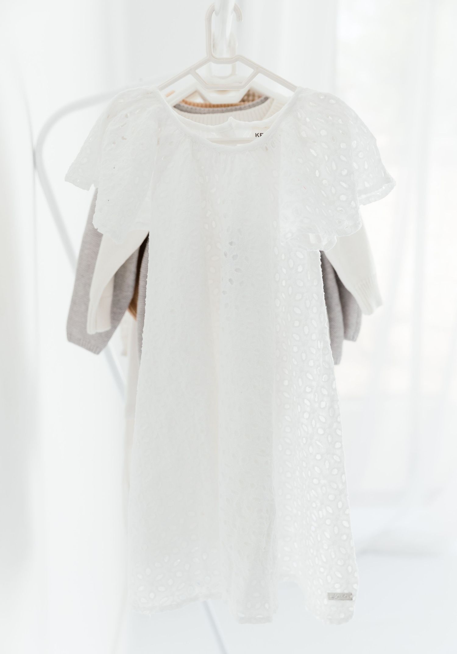 White eyelet lace short sleeve girls dress hanging on a white hanger against a light background.