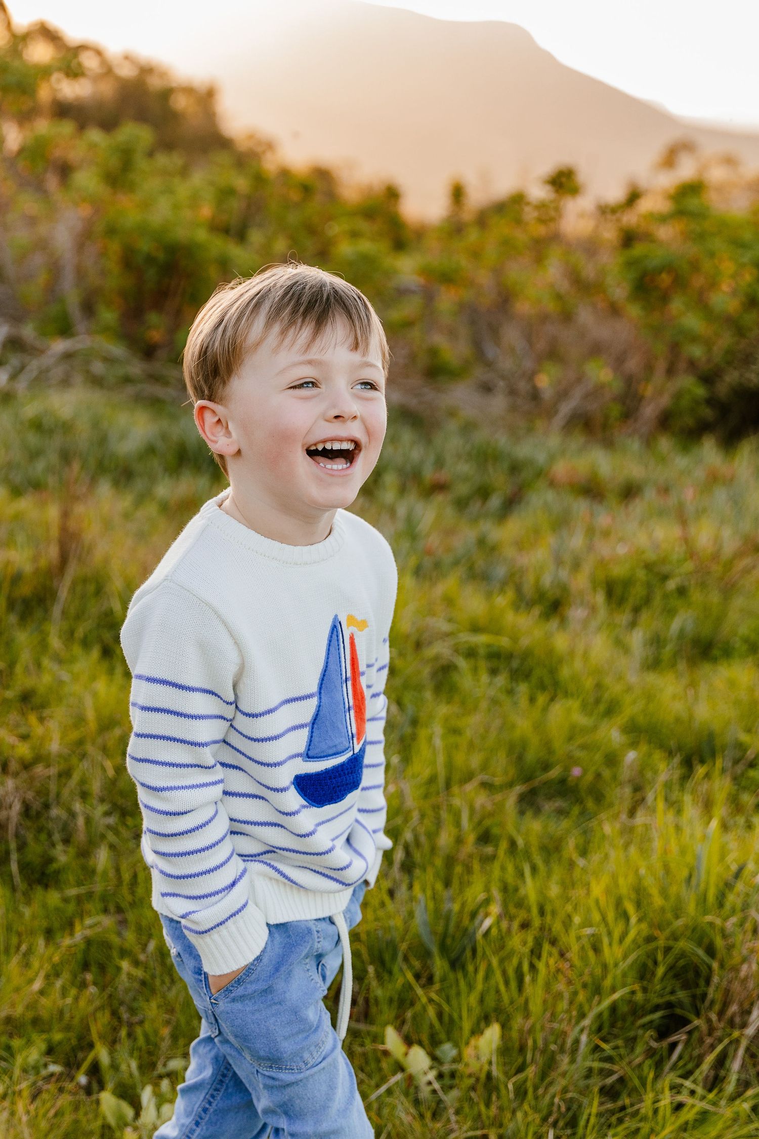 Cheerful young boy in a sailboat sweater smiling and walking in a sunny meadow.