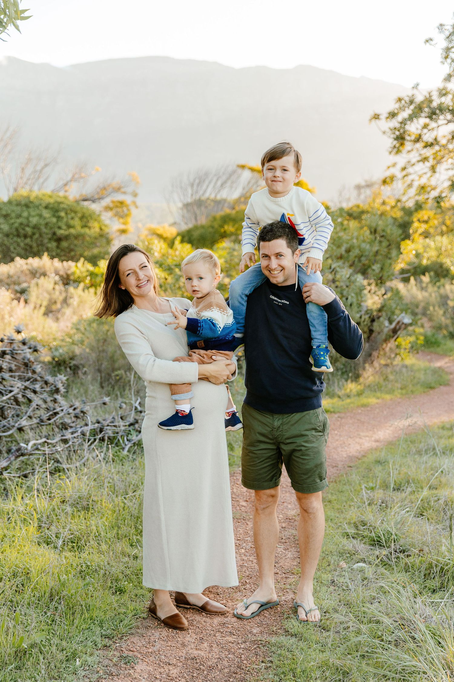 Smiling family of four poses on a scenic mountain trail during golden hour light.