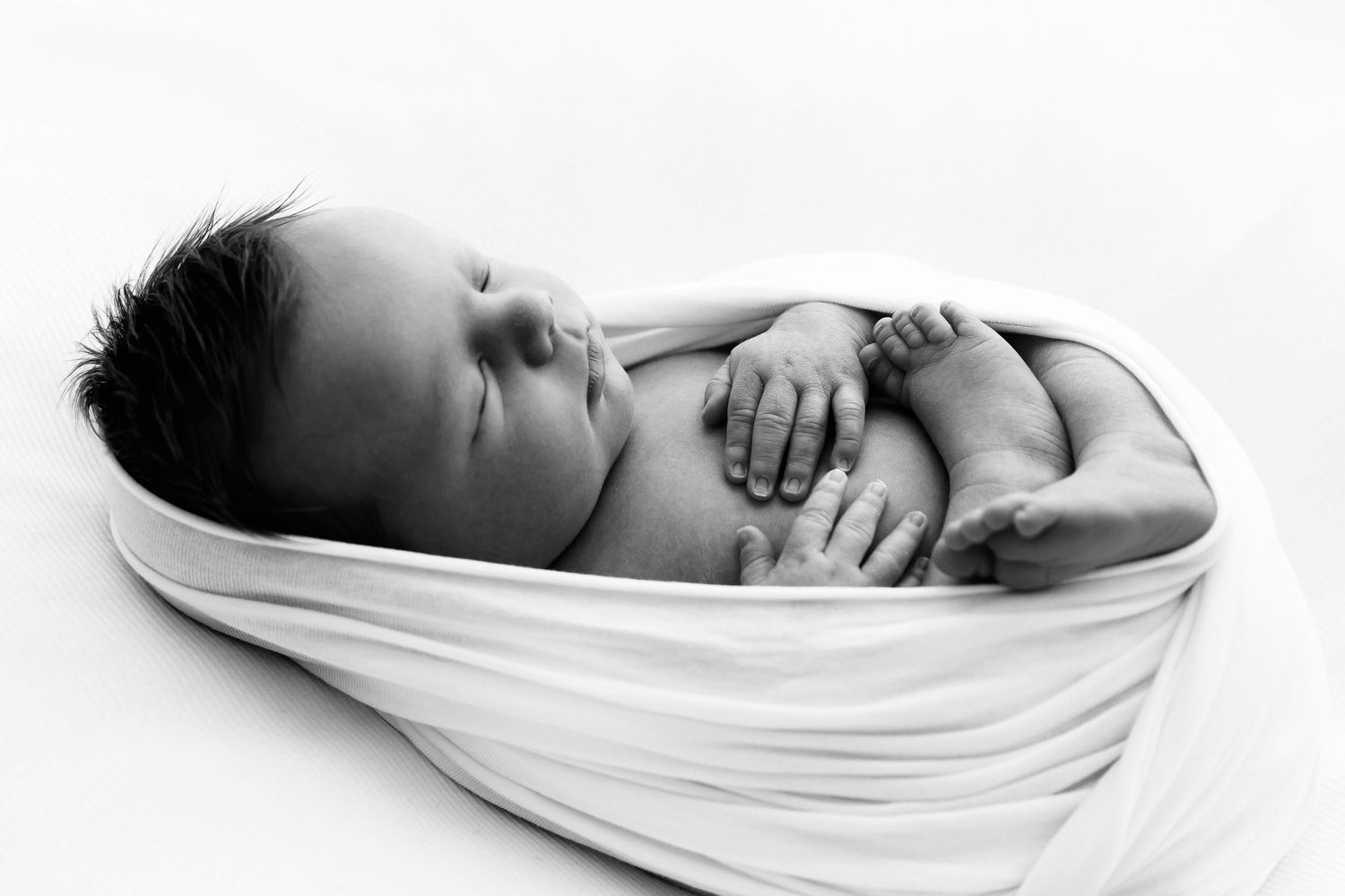 A peaceful sleeping newborn wrapped in white fabric against a white background.