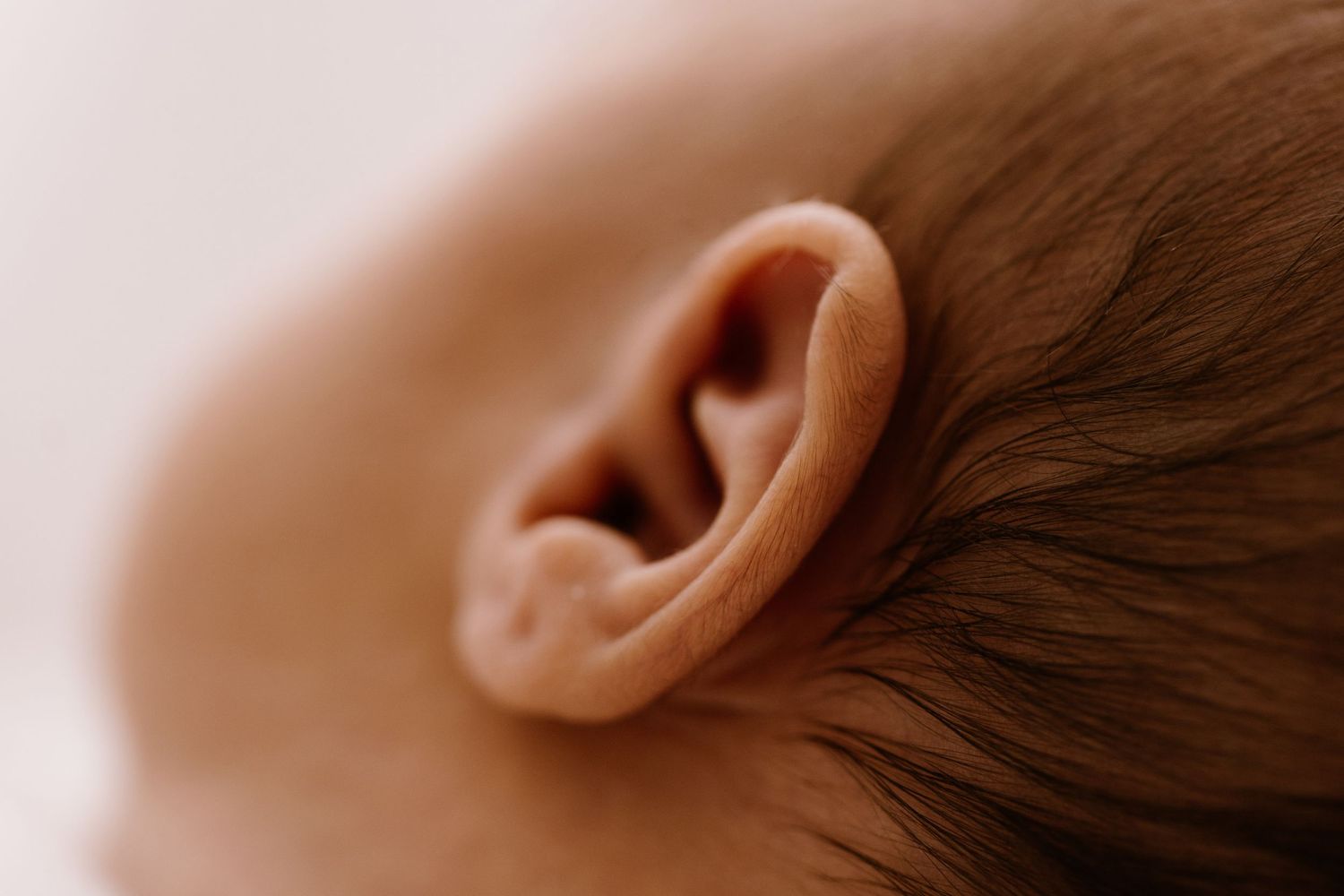 Close-up macro photo of a newborn baby's ear with fine hair, soft skin texture in warm tones.