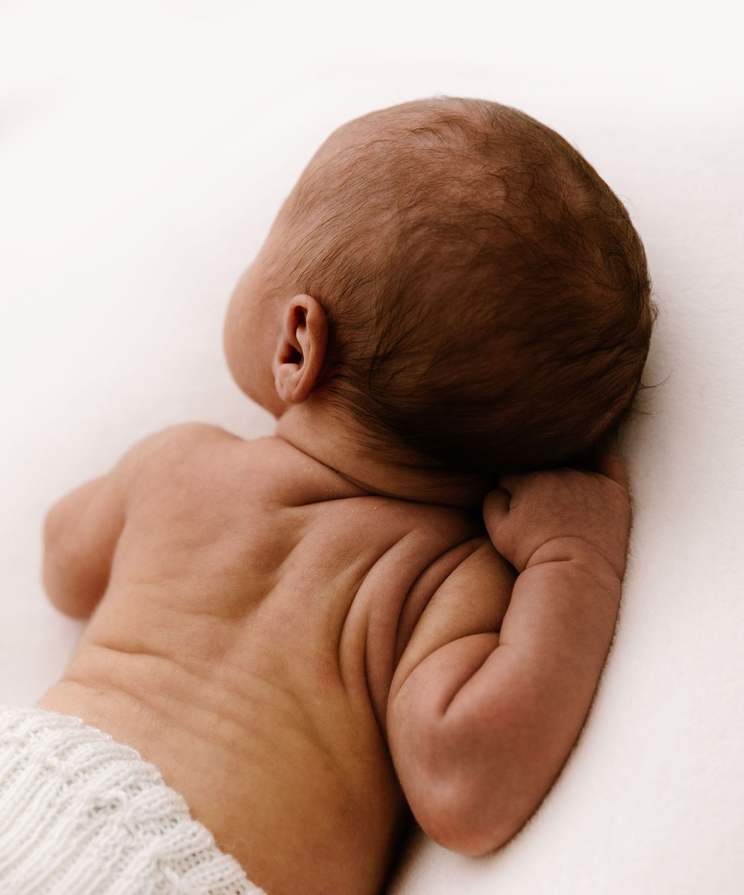 Close-up of a newborn baby lying on its back, with an adult hand gently supporting its head.