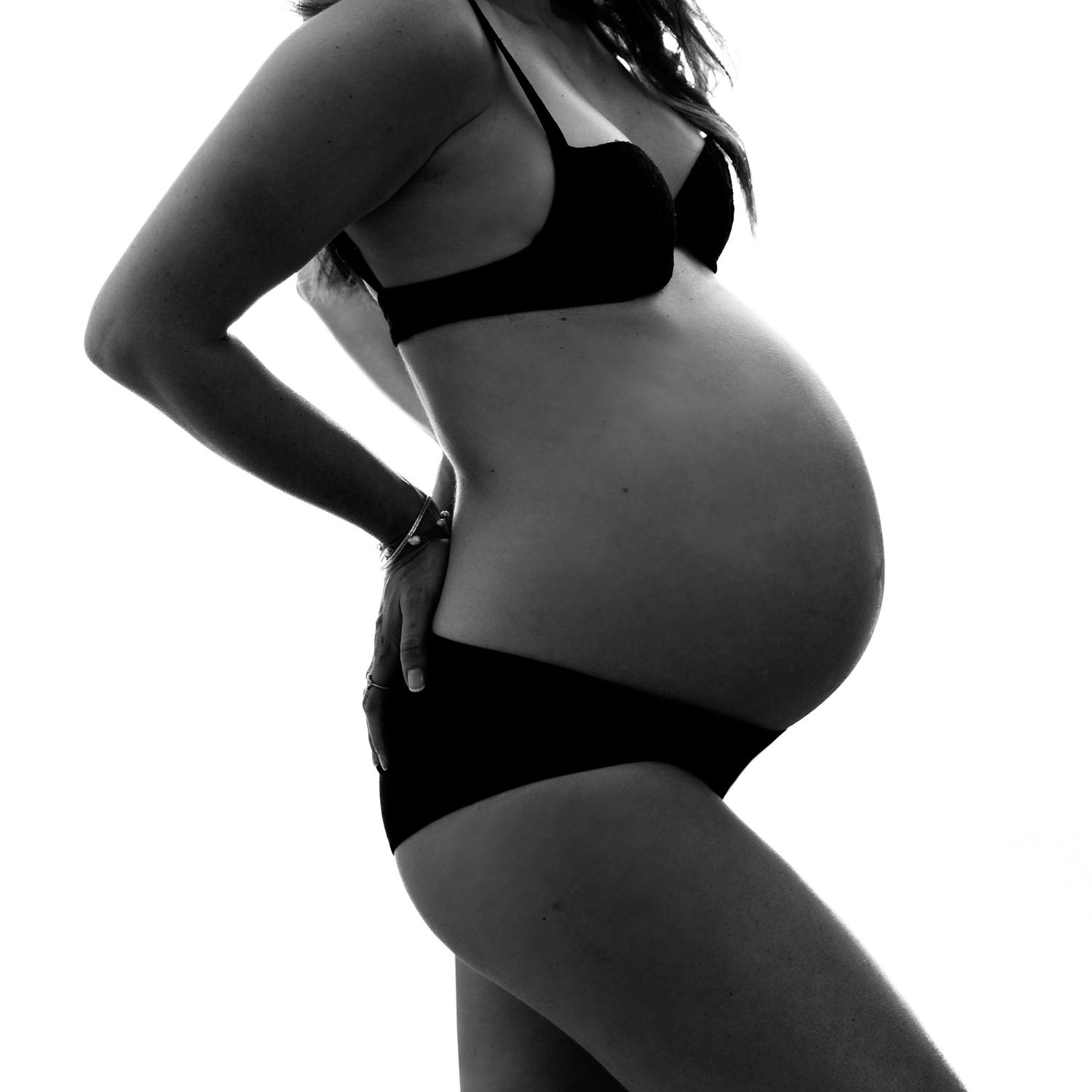 Black and white photo of a pregnant woman in black lingerie showing her baby bump, side profile maternity shot.