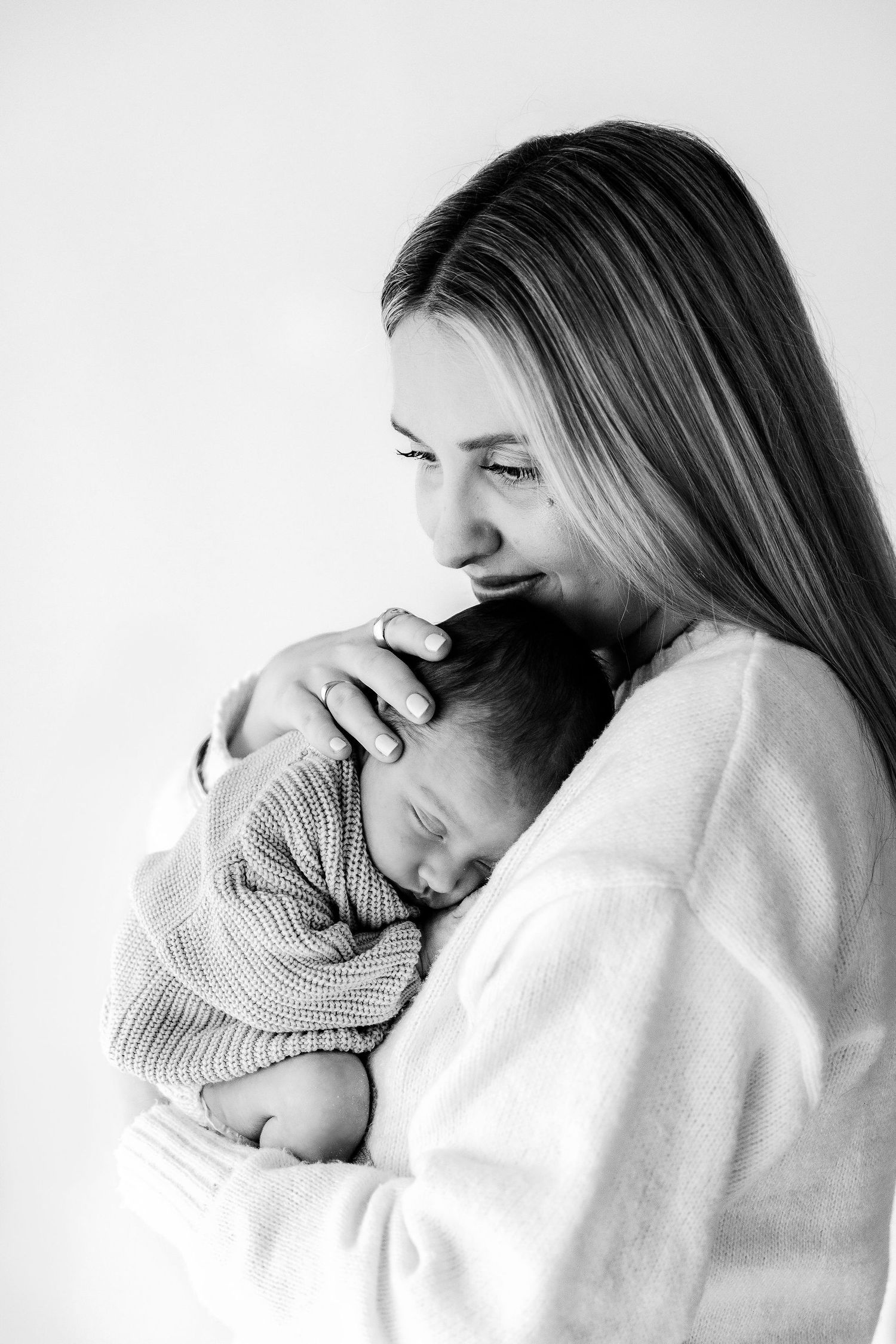 Black and white portrait of a mother tenderly holding her sleeping newborn baby close to her chest.
