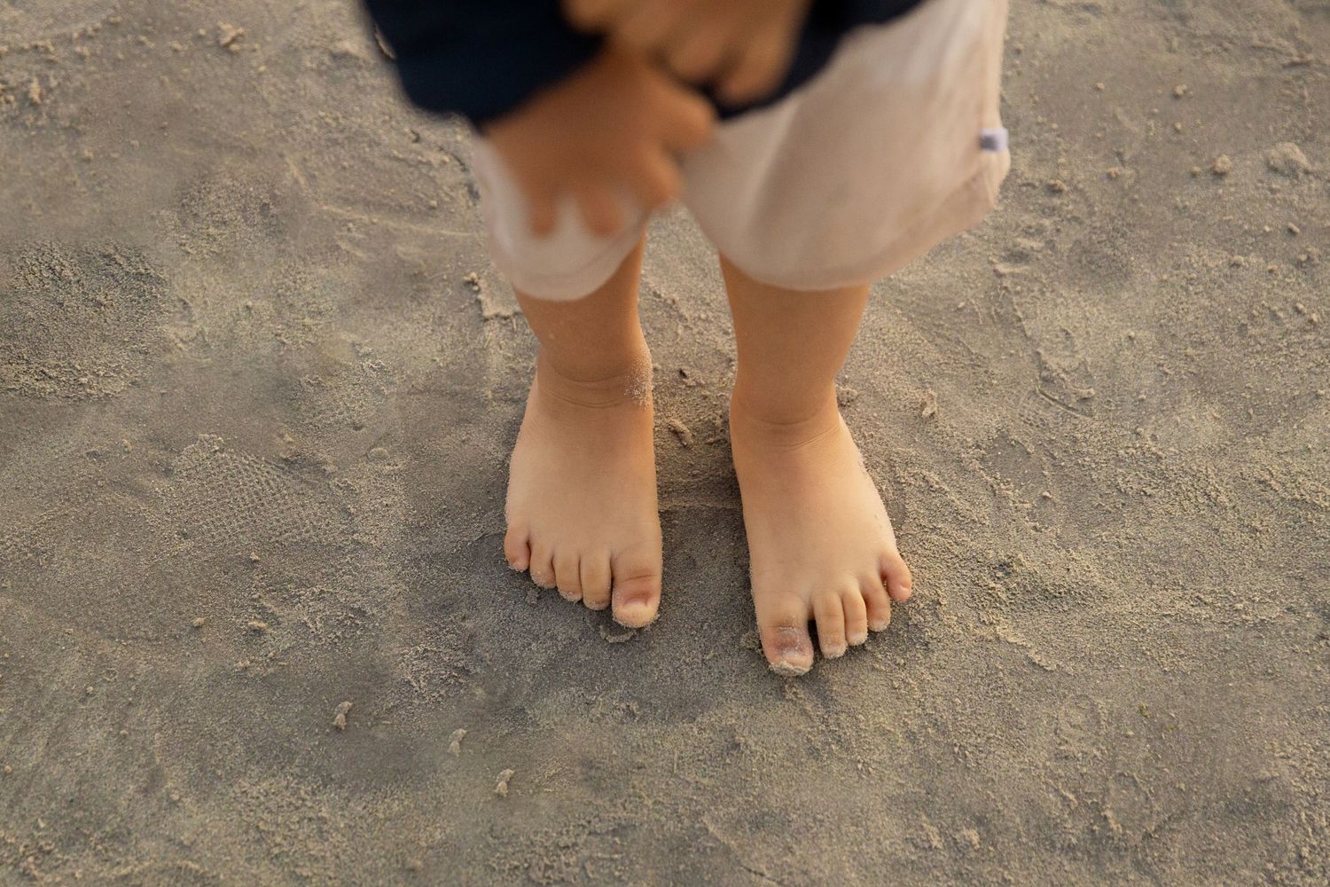 Child's bare feet standing on sandy beach, top-down view of young kid's toes in sand.