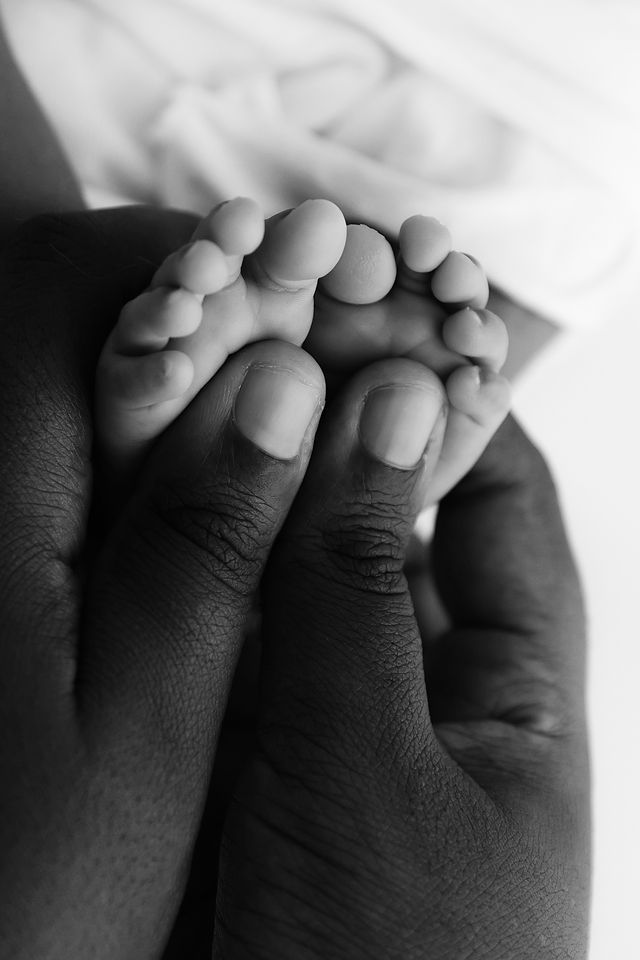 Close-up black and white photo of a newborn baby's tiny feet resting in a parent's hands.