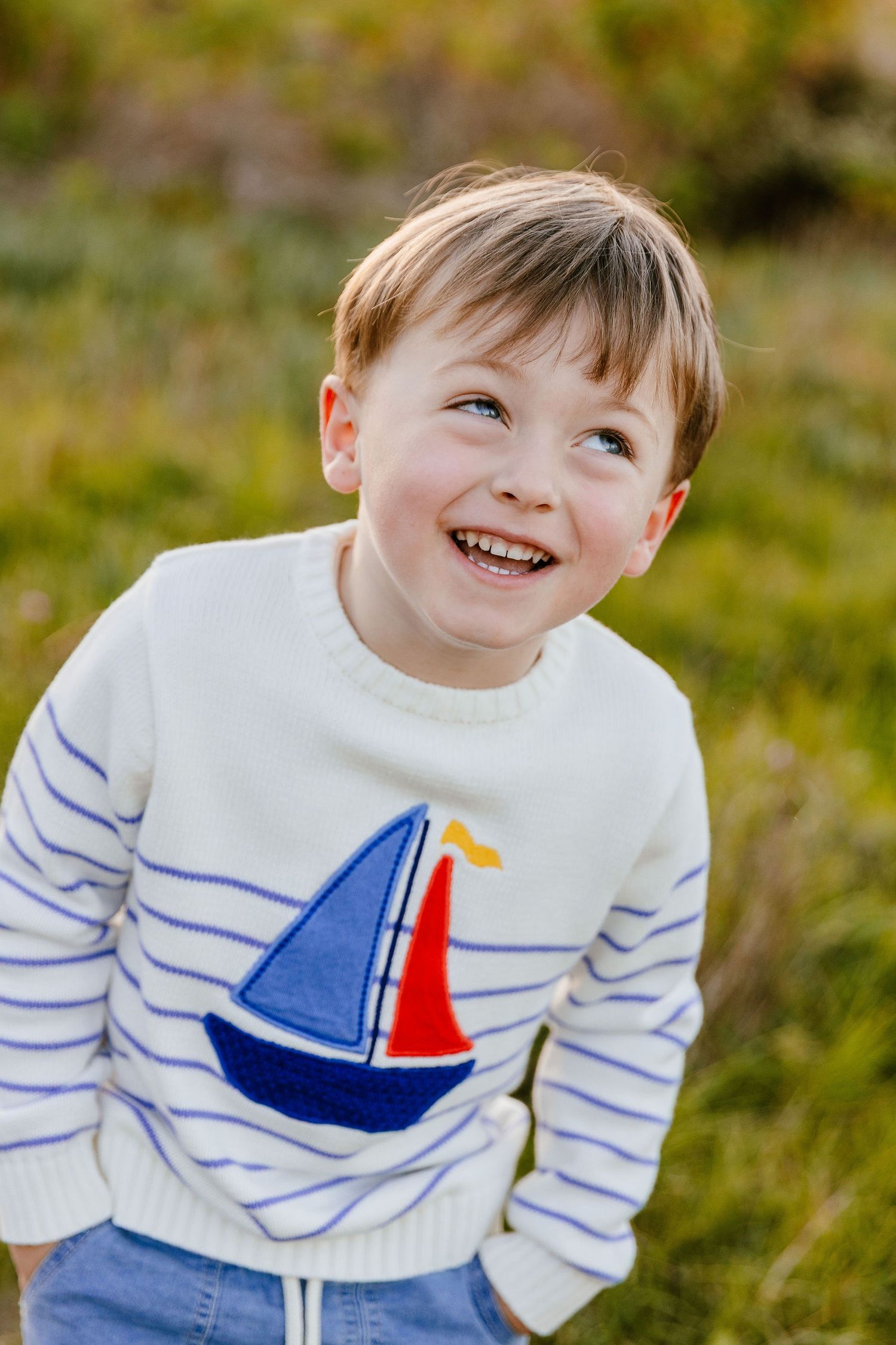 Happy young boy in striped sailboat sweater laughing outdoors in a grassy field.