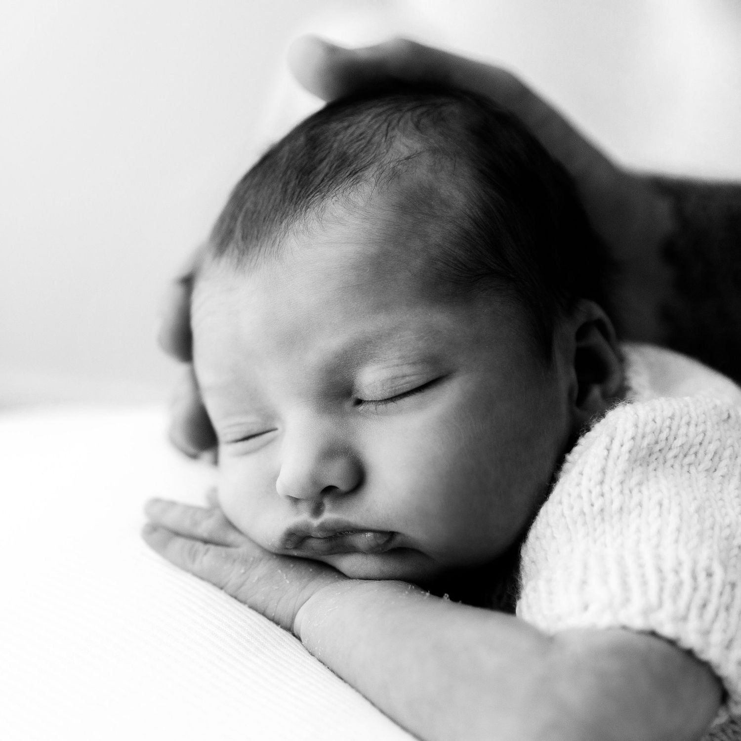 Black and white photo of sleeping newborn baby gently supported by parent's caring hands.