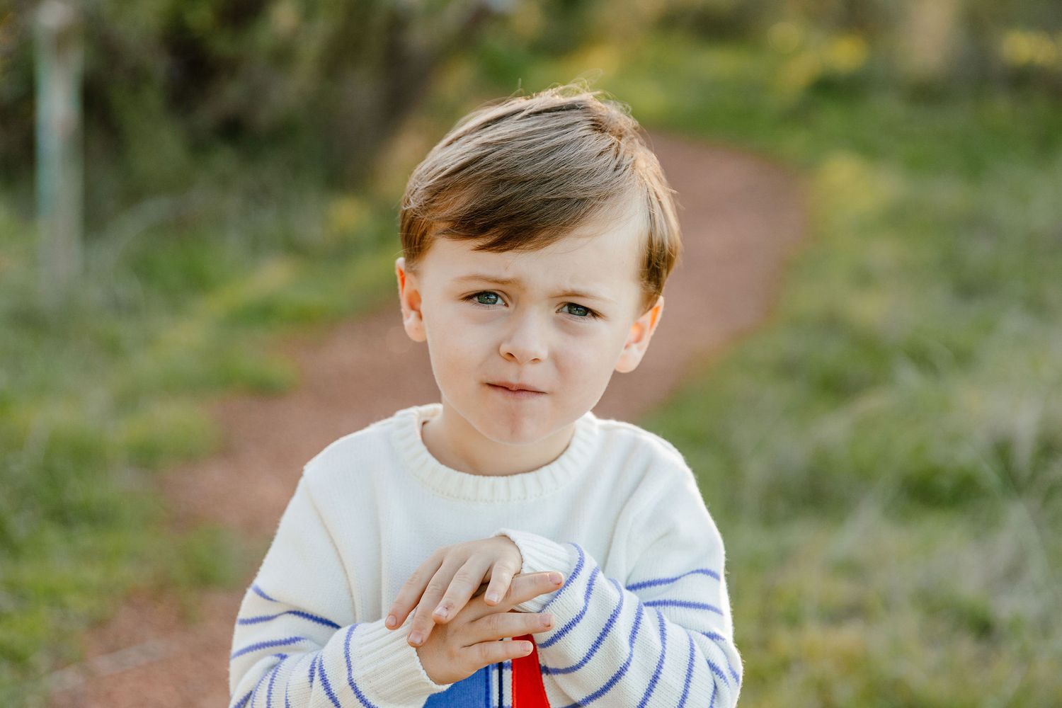 Young boy in white striped sweater holding colorful toy on outdoor path.