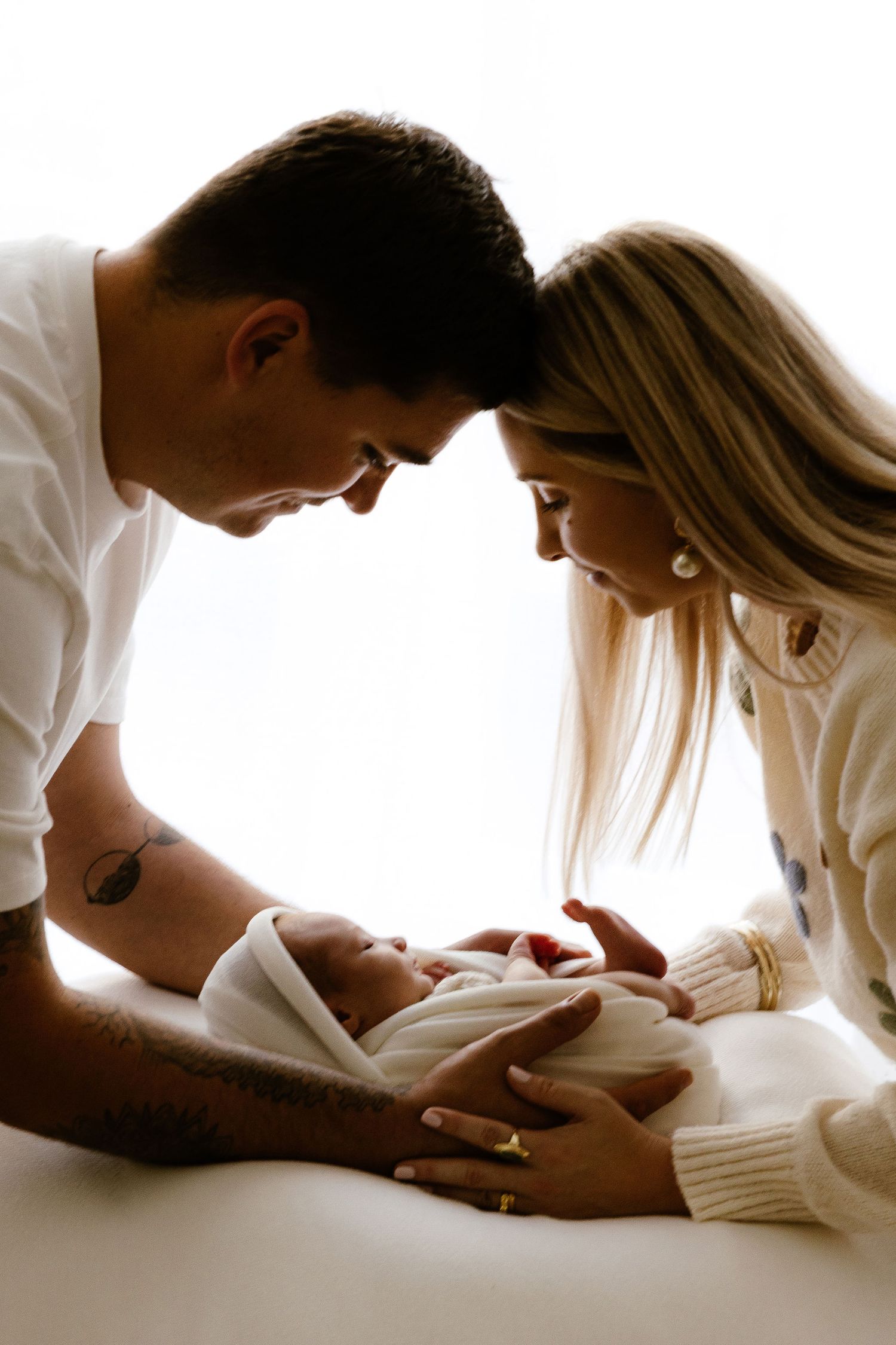 Loving parents leaning over their swaddled newborn baby in a tender family portrait.