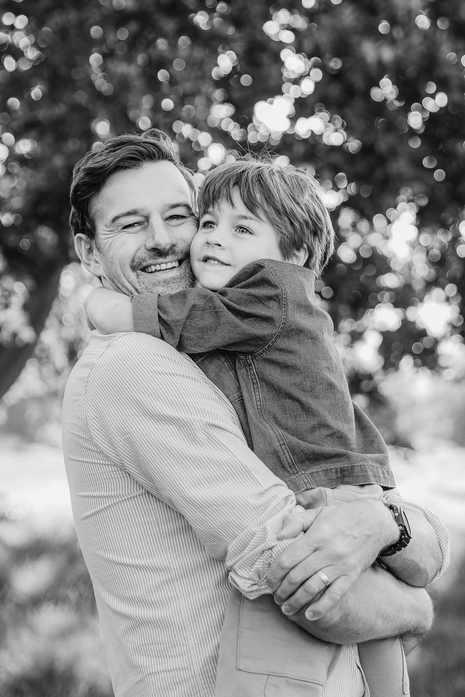 Black and white photo of a smiling man holding a happy young boy in an outdoor park setting.